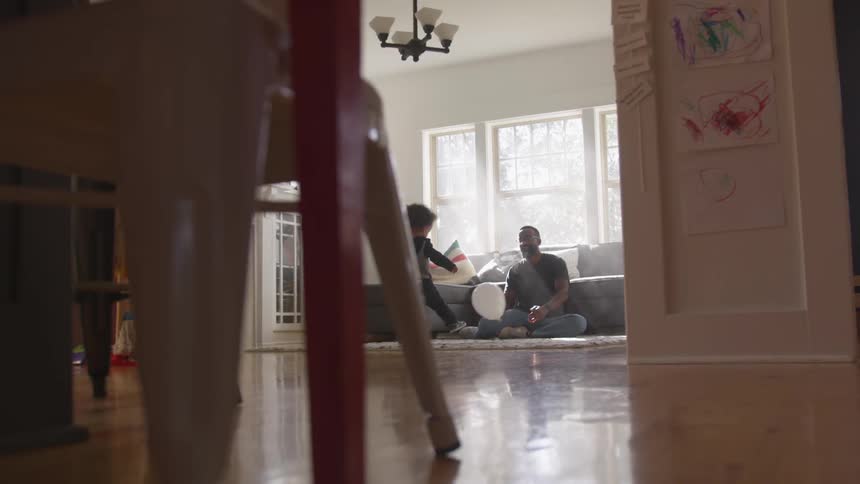A man plays with a boy on the living room floor with a white balloon