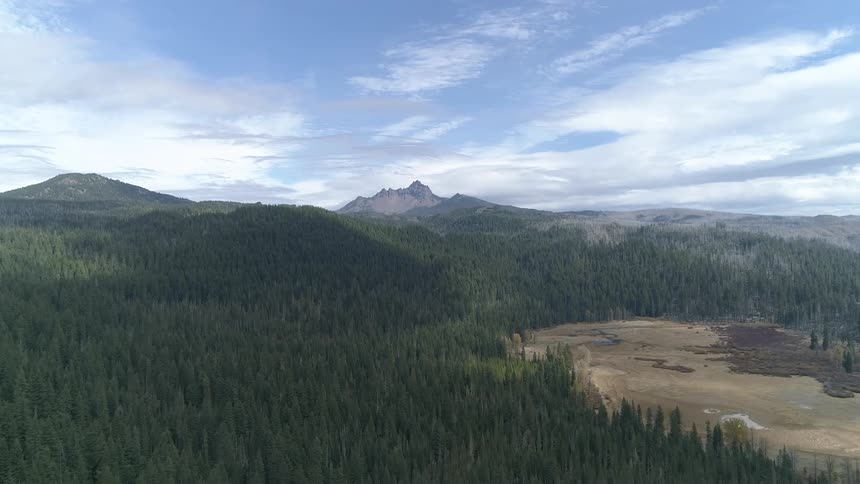 A flat clearing is nestled in the middle of a hilly forest