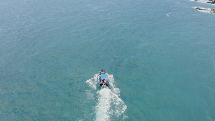 Speed boat cuts through blue water near the shore