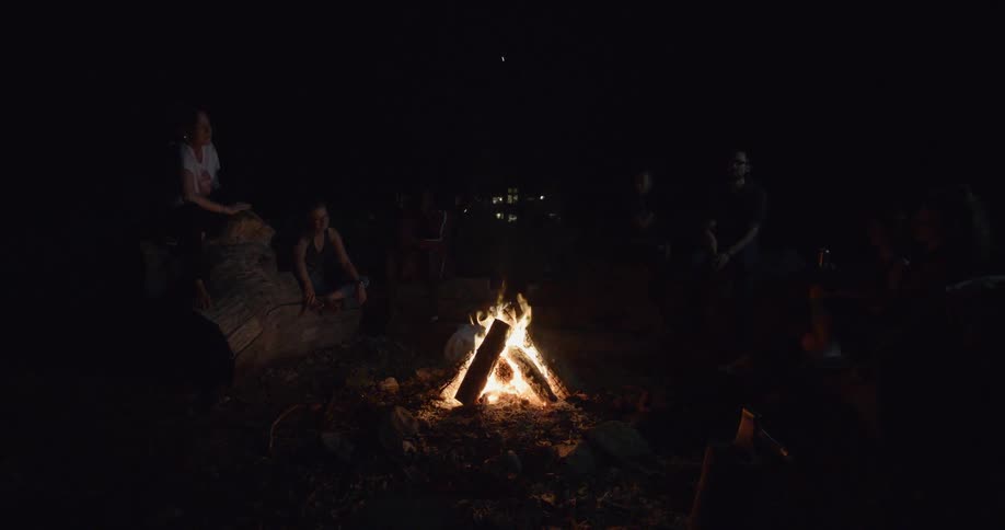 A group of people hanging out in front of a camp fire