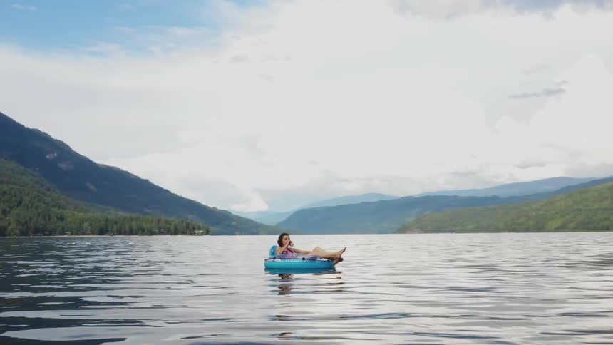Woman floats on inner tube in middle of lake surrounded by mountains