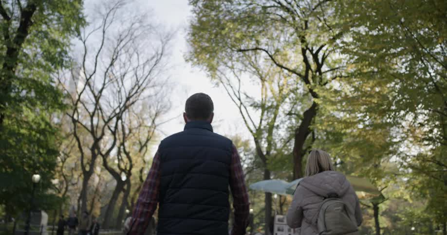 Man and woman walk along path in park past umbrella covered tables