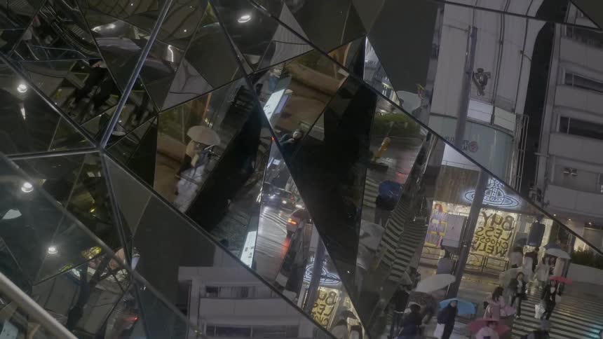 A mirrored skyscraper shows reflections of pedestrians crossing the street below