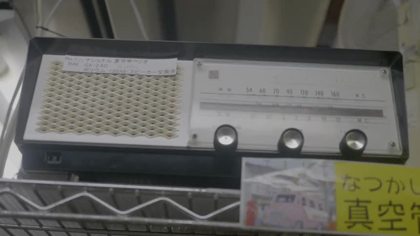 An old radio sits on a store shelf with a sign in front of it written in an asian language