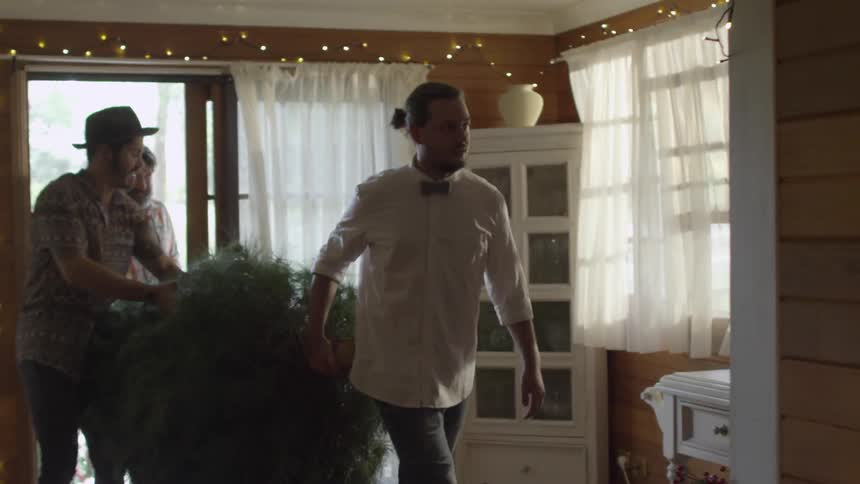 Three men carry a christmas tree into a house