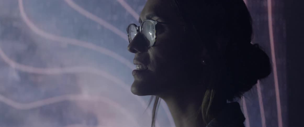 A woman with glasses is standing next to a video wall