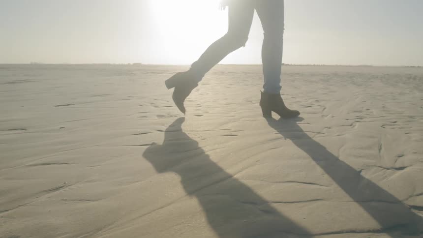A woman with heels walks on the sand