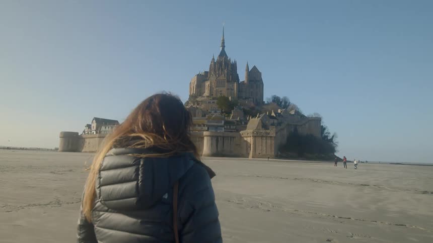 A woman in a coat walking towards mont saint michel