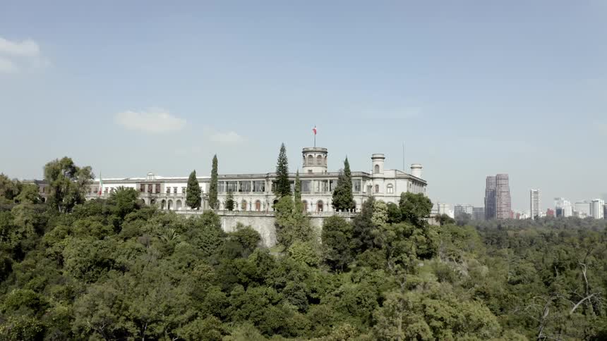 A building with a flag surrounded by trees with a city in the background