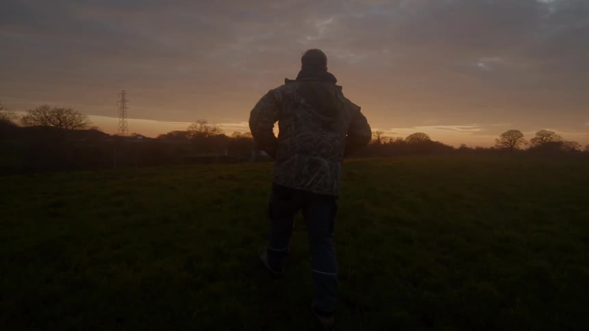 A man in a coat walking through a field at sunset