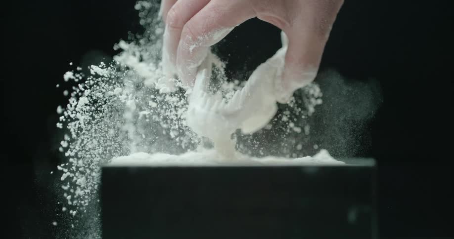 The hand of a man reaches into a container of powdery material before pulling out a small replica of a dinosaur jawbone