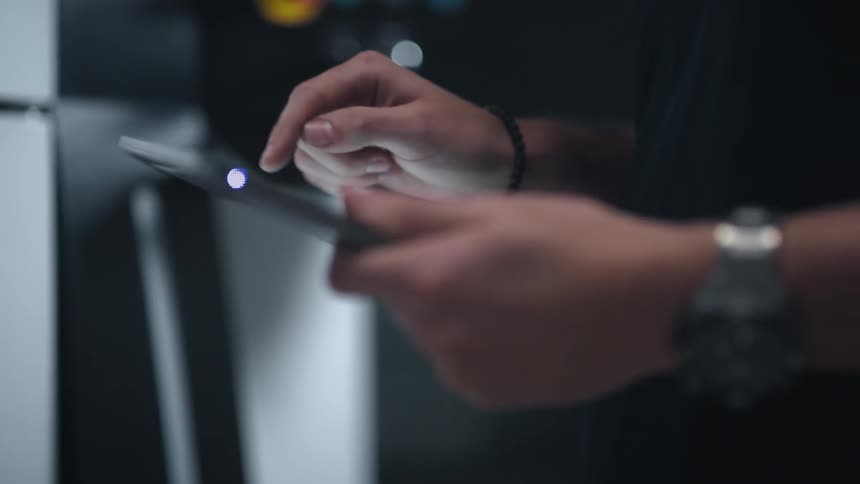 A person standing indoors taps on the surface of an electronic tablet