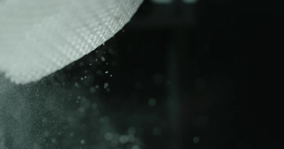 A piece of woven mesh fabric that is hanging is shaken which releases a cloud of white powder