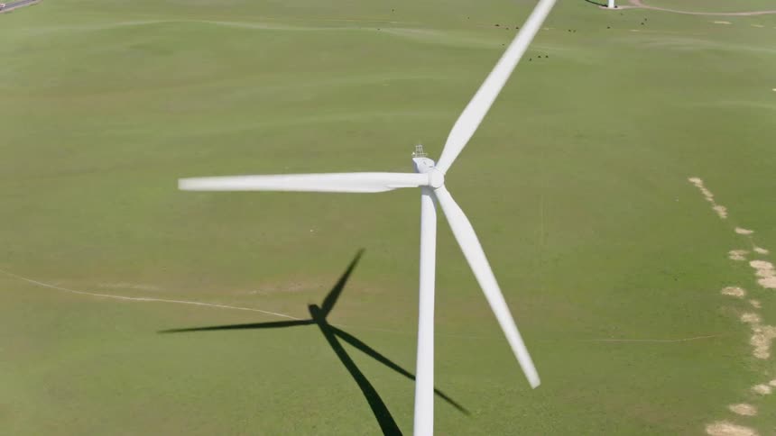 A wind turbine rotates on flat grassland