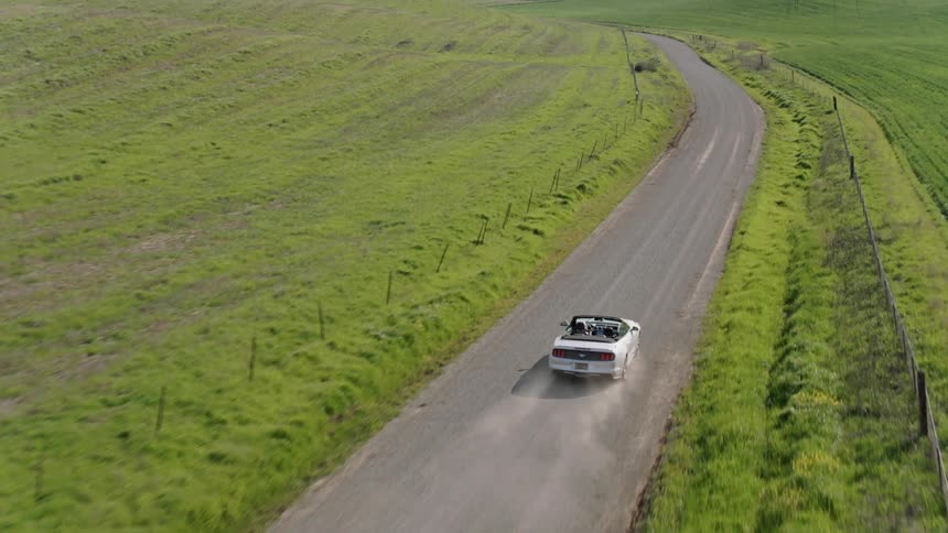 Aerial of a white car driving on country road in the daytime