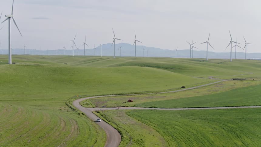 A car drives down a winding road on a wind farm