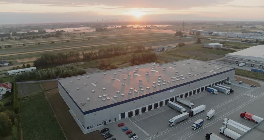 A warehouse with trucks with fields and the sky in the background