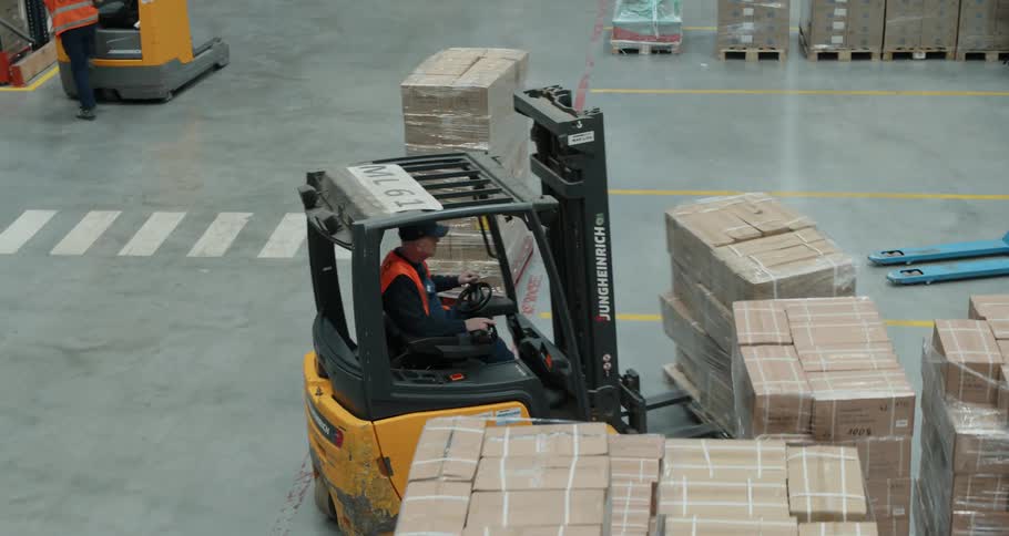 A person drives a full forklift inside a door to a trailer