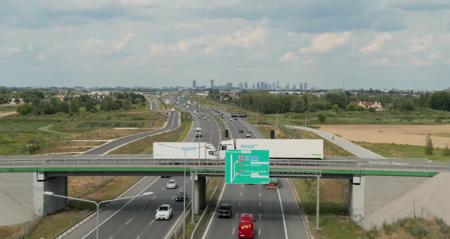 Two trucks drive on an overpass over a busy interstate