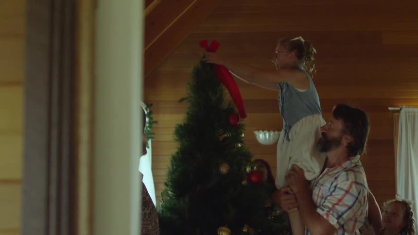 A man picking up a girl and helping her put a bow on a christmas tree