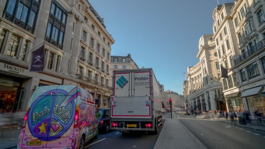 Personal and public vehicles drive on a city street surrounded by businesses