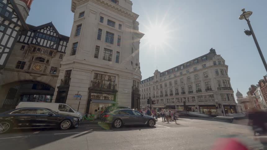 People and cars move through a busy city intersection on a bright sunny day