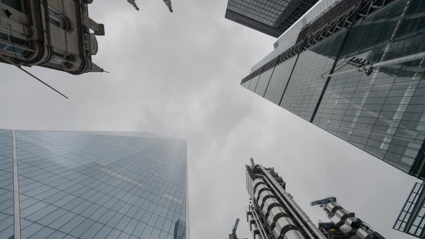 A group of towering sky scrapers and buildings with unique architecture loom overhead on a cloudy day