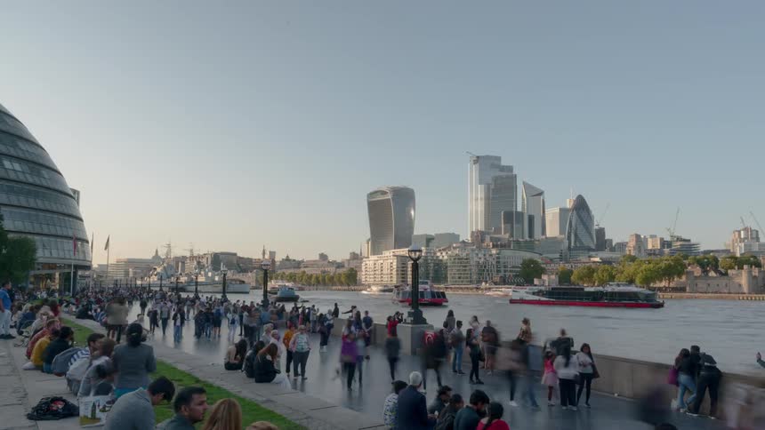 Hundreds of people travel a pedestrian walk area beside a river