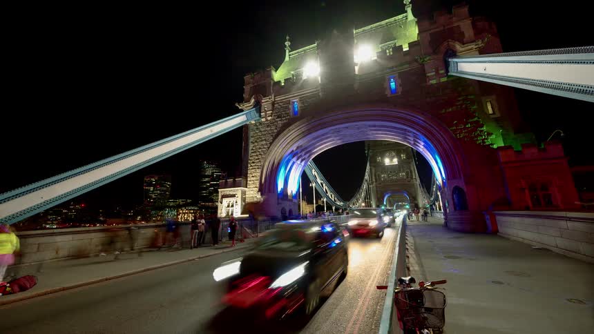 Pedestrians and traffic travel under the lit bridge at night