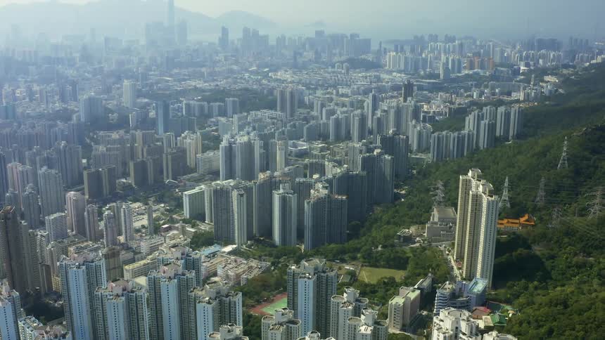 An urban area with densely packed skyscrapers is next to a hilly area covered with trees