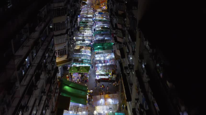 A road between tall buildings is filled with business stalls at night