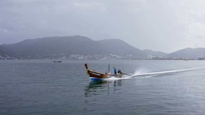 A long wooden motor boat moves through the water leaving a wake