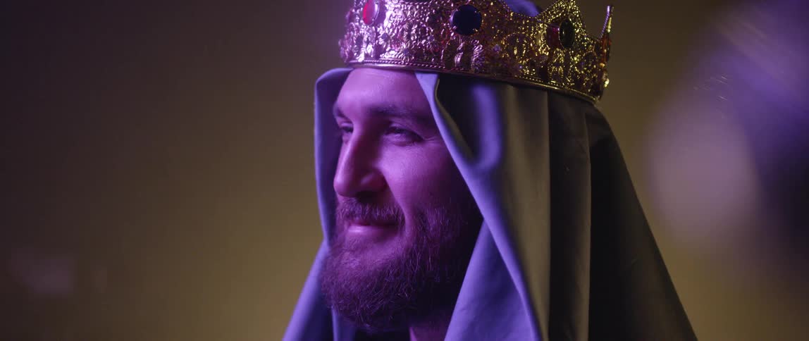 A man wearing a cloth head cover and a gold and jeweled crown smiles