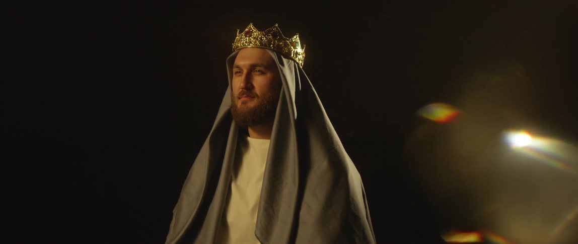 A man with a beard wears a crown over a cloth on his head