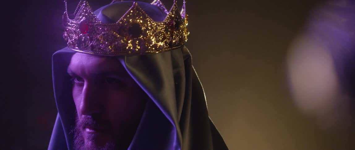 A man with a headcover and a crown staring into the distance