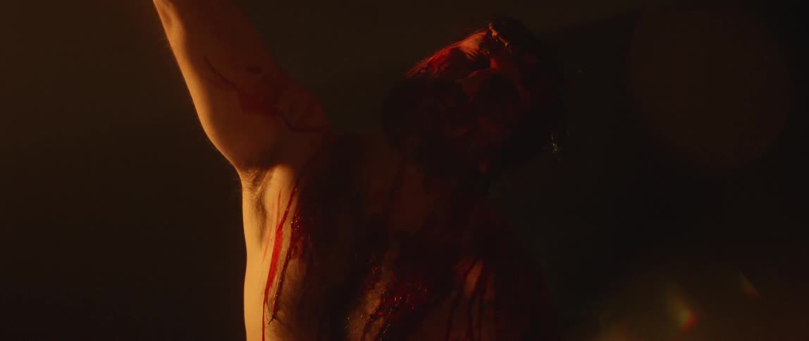 A man with blood dripping down his body raises his arm in the air