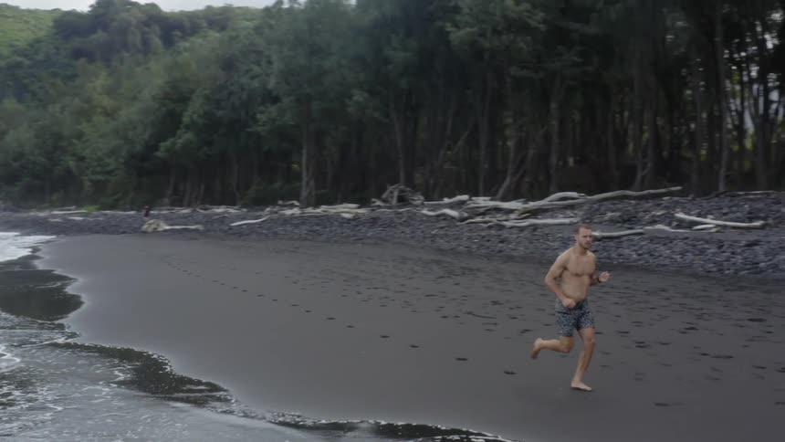 Shirtless man running barefoot on the beach alongside the shoreline