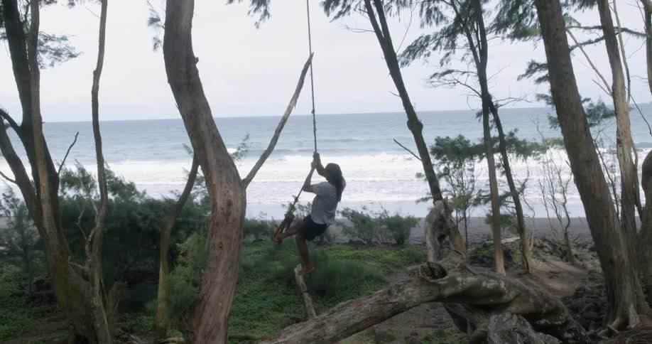A man swings on a rope hung from a tree near the beach