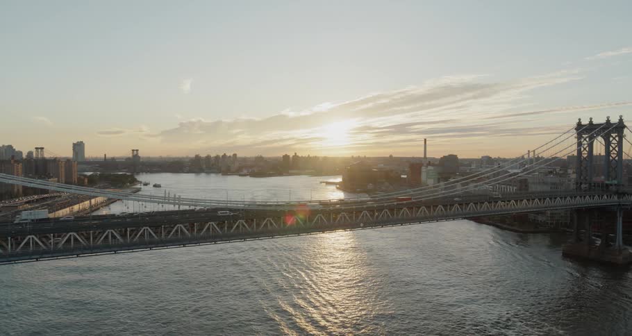 Cars and trucks travel across a city bridge over a river at sunrise