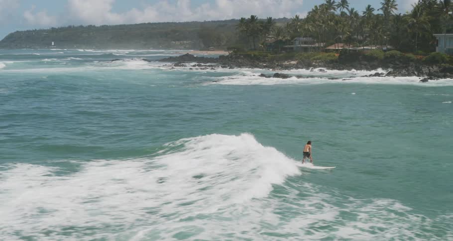 A man on a surfboard catches a small wave at his back and rides it a bit towards shore in a tropical location