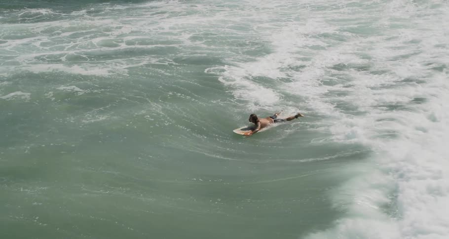 A man swims on a surfboard through large ocean waves
