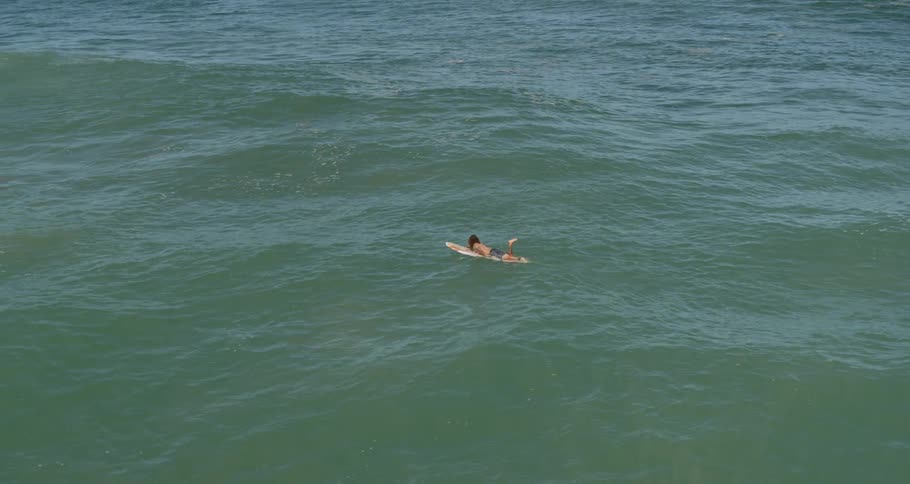 Male laying on his stomach on a surfboard in the ocean paddles with his arms out to meet the waves