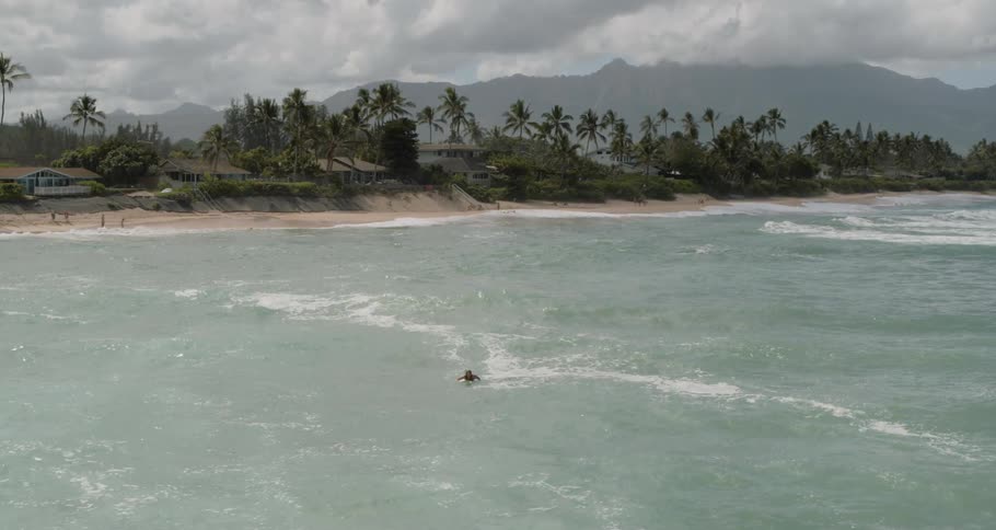 Man swims on surfboard to surf waves in the sea during daylight