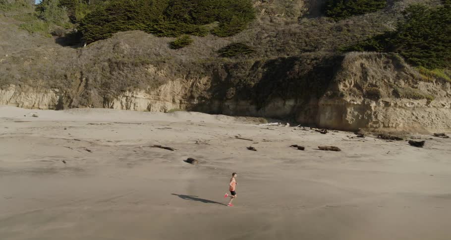 A man running in the beach with cliffs in the background