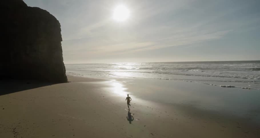 Man runs on the wet sand beach next to the ocean in the afternoon