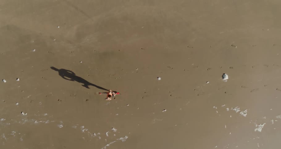 A man jogs on sand as the wind blows white debris around on a sunny day