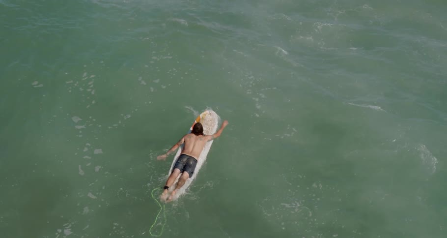 A male paddles himself on his surfboard over green ocean water