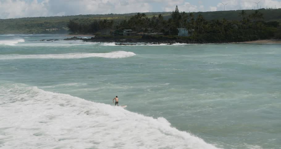 A surfer rides a wave in pale blue tropical waters