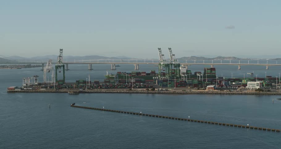 A shipping port full of containers and cranes sits alongside a bridge