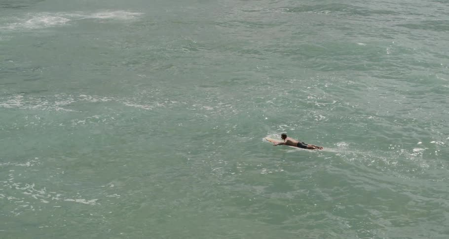 A surfer paddles against the current
